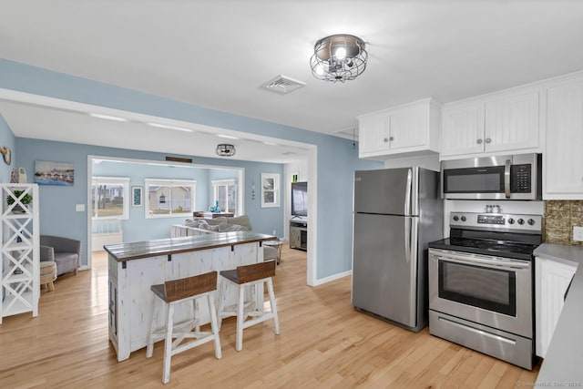 37 Woodland Dr, Old Saybrook, CT 06475 - kitchen with appliances with stainless steel finishes, light wood finished floors, white cabinetry, open floor plan, and a kitchen breakfast bar