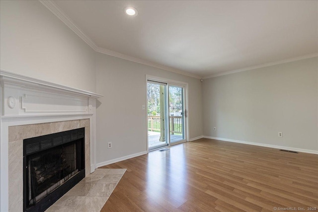 unfurnished living room with a tiled fireplace, light wood-style flooring, baseboards, and ornamental molding