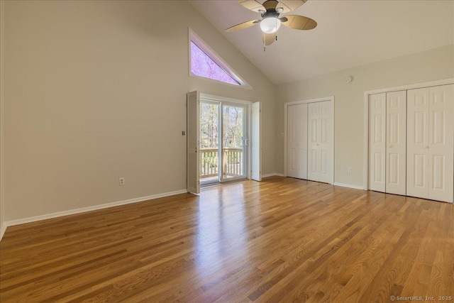 unfurnished bedroom featuring baseboards, access to outside, high vaulted ceiling, and multiple closets