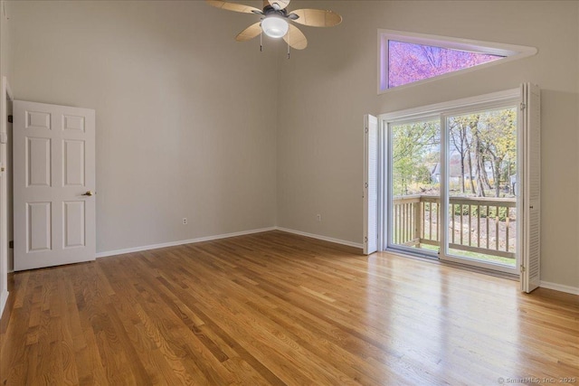 spare room with light wood finished floors, a ceiling fan, baseboards, and a towering ceiling