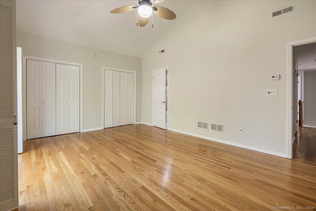 unfurnished bedroom with light wood-style floors, visible vents, two closets, and high vaulted ceiling