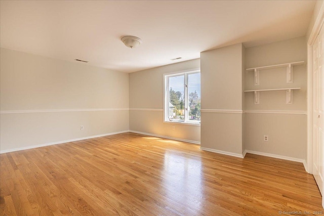 empty room with light wood finished floors, baseboards, and visible vents