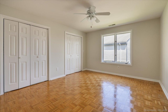 unfurnished bedroom featuring two closets, baseboards, ceiling fan, and visible vents