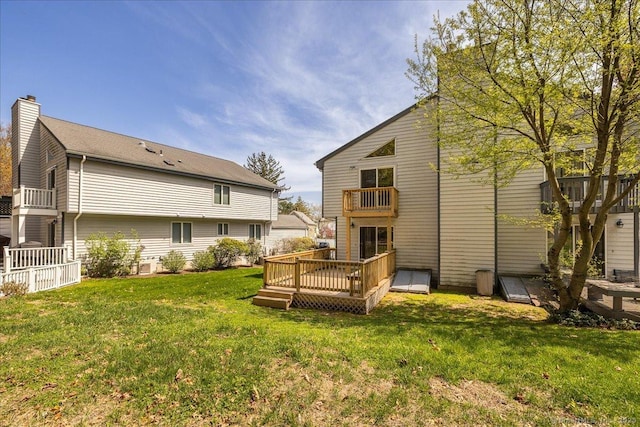 rear view of house featuring a balcony, a chimney, a wooden deck, and a lawn