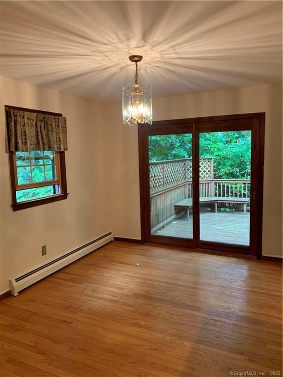 empty room featuring a notable chandelier, wood finished floors, and baseboard heating