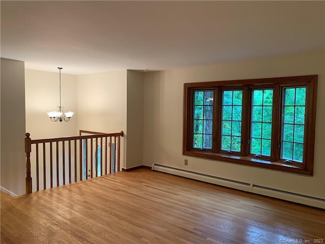 empty room featuring a chandelier, baseboard heating, baseboards, and wood finished floors