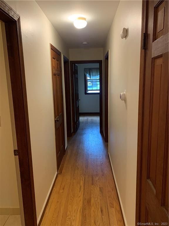 corridor with light wood-style flooring and baseboards