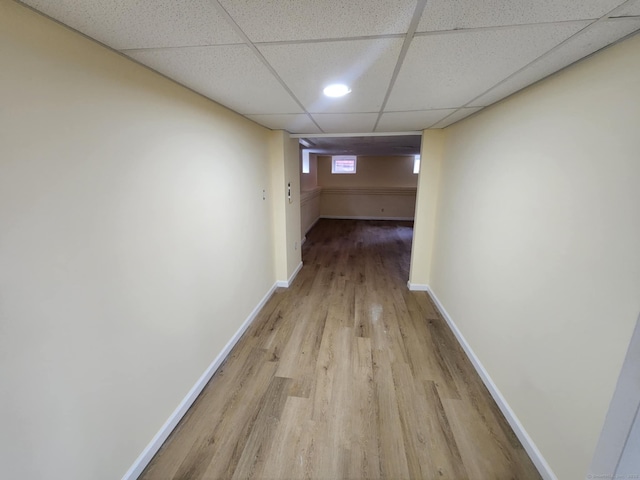 corridor with baseboards, light wood-style flooring, and a paneled ceiling
