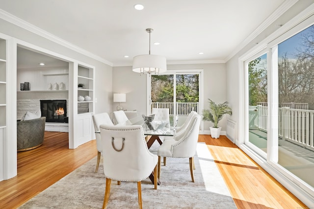 dining room featuring light wood-style flooring, crown molding, a glass covered fireplace, and recessed lighting