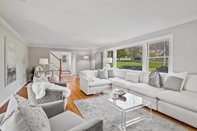 living room featuring stairs, light wood-style flooring, baseboards, and crown molding