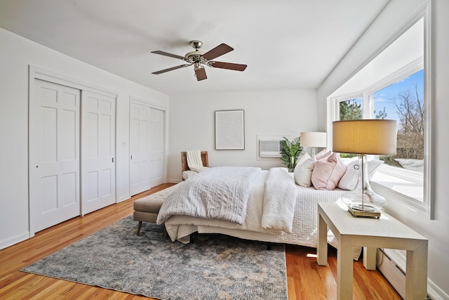 bedroom featuring baseboards, two closets, a ceiling fan, and wood finished floors