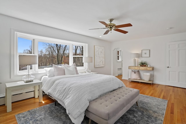 bedroom featuring ceiling fan, light wood finished floors, and a baseboard heating unit