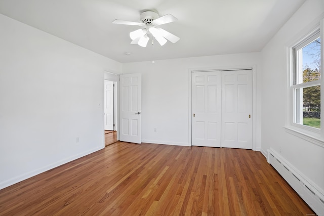 unfurnished bedroom with multiple windows, a baseboard radiator, and light wood-type flooring