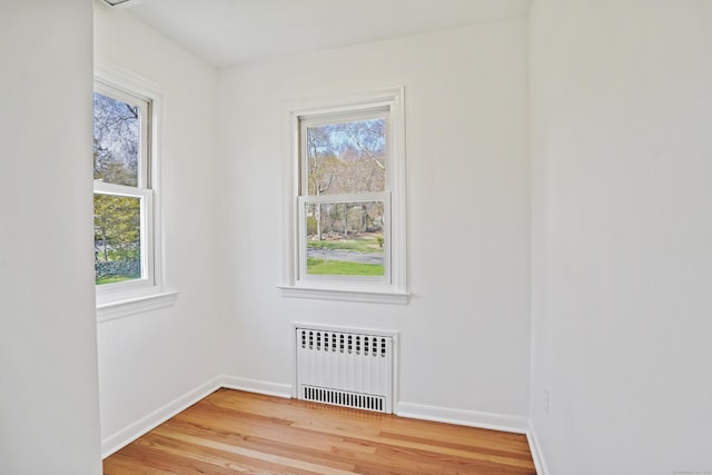 spare room with radiator heating unit, baseboards, and wood finished floors
