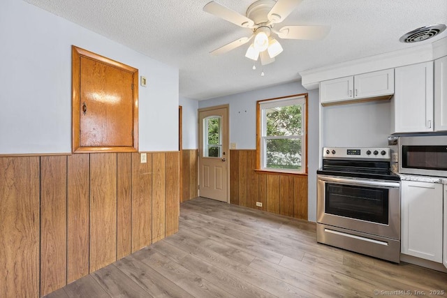287 Prospect St, Wethersfield, CT 06109 - kitchen featuring appliances with stainless steel finishes, wainscoting, wood walls, a textured ceiling, and light wood-style floors