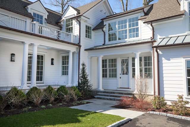 view of exterior entry with a balcony, a standing seam roof, a shingled roof, and covered porch