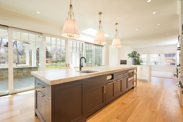 kitchen featuring a sink, decorative light fixtures, an island with sink, light wood-style flooring, and light countertops