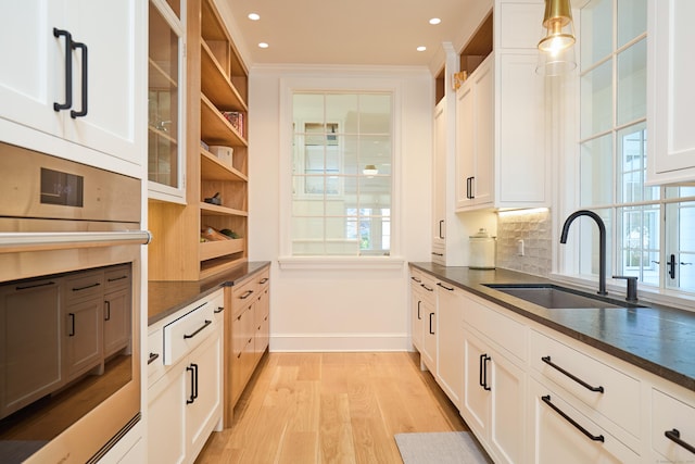kitchen with dark countertops, light wood-style flooring, stainless steel oven, and a sink