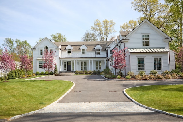 view of front of property with curved driveway, a front lawn, a standing seam roof, and a balcony