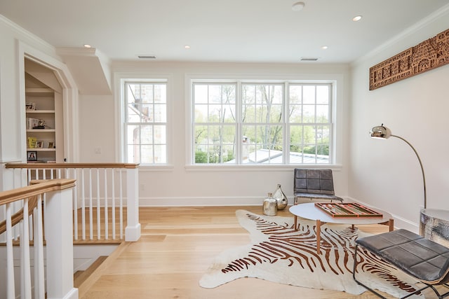 sitting room with ornamental molding, plenty of natural light, and wood finished floors