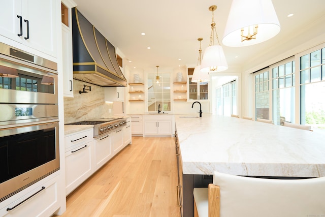 kitchen with light wood-style flooring, a sink, custom range hood, backsplash, and appliances with stainless steel finishes