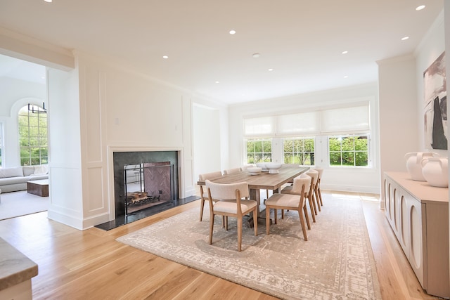 dining room featuring a healthy amount of sunlight, crown molding, light wood finished floors, and a fireplace with flush hearth