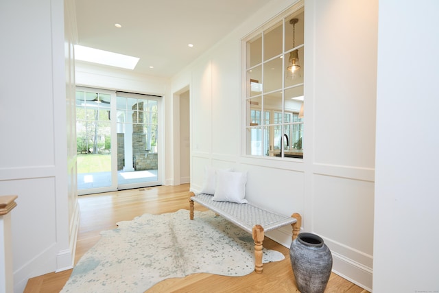 sitting room with light wood-style floors, a decorative wall, and a skylight