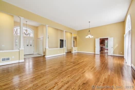 unfurnished living room with visible vents, a wealth of natural light, wood finished floors, and a notable chandelier