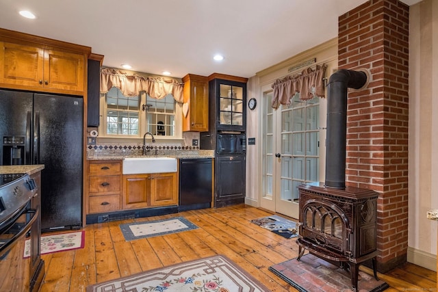 120 Boston Post Rd, Old Lyme, CT 06371 - kitchen with black appliances, a wood stove, light wood-type flooring, brown cabinets, and light stone countertops