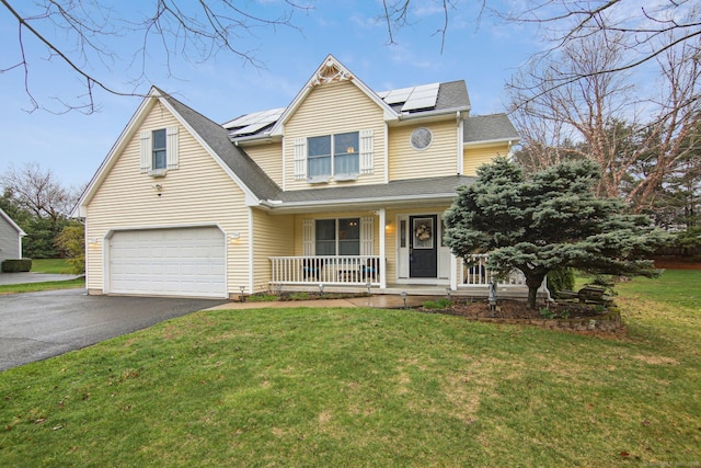 traditional home featuring a porch, a front yard, solar panels, a garage, and driveway