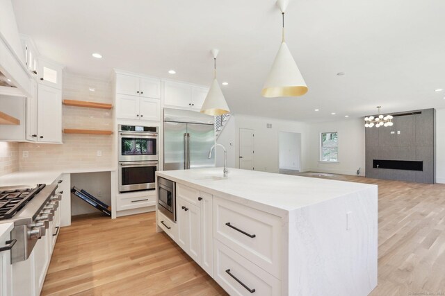 kitchen featuring built in appliances, light wood-type flooring, backsplash, open shelves, and white cabinets