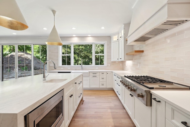 kitchen with custom exhaust hood, appliances with stainless steel finishes, a sink, and white cabinetry