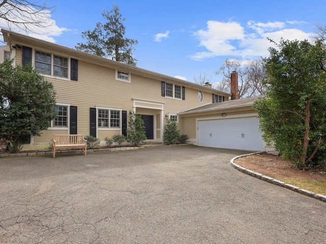 colonial inspired home featuring an attached garage, a chimney, and aphalt driveway