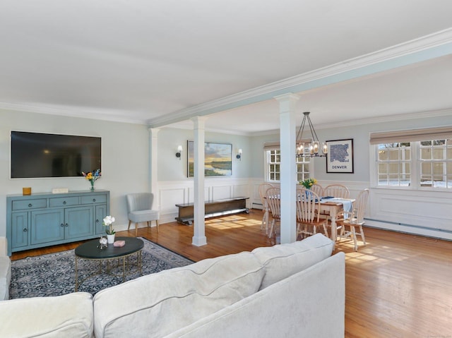 living room featuring crown molding, an inviting chandelier, decorative columns, and wood finished floors
