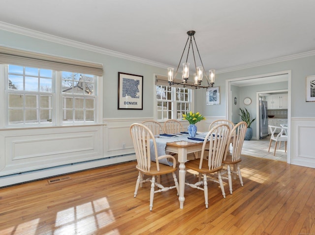 dining area featuring crown molding, light wood finished floors, a wainscoted wall, and an inviting chandelier