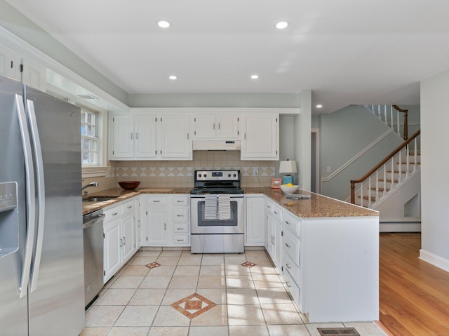 kitchen with decorative backsplash, a peninsula, under cabinet range hood, a sink, and stainless steel appliances