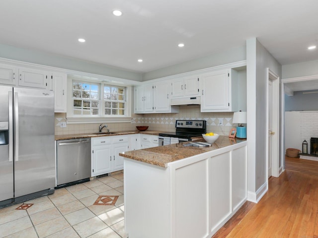 kitchen featuring backsplash, a sink, white cabinets, under cabinet range hood, and stainless steel appliances
