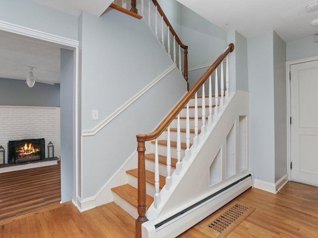 staircase featuring baseboards, a baseboard heating unit, wood finished floors, and a fireplace