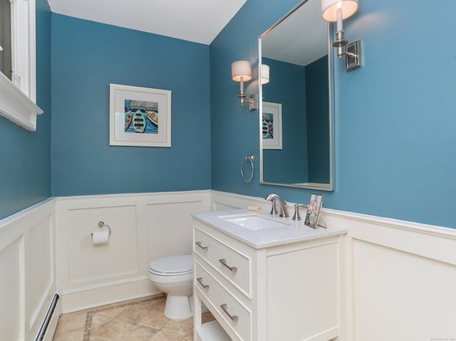 bathroom featuring wainscoting, a decorative wall, a baseboard heating unit, and toilet