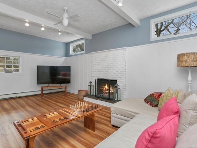 living room featuring a brick fireplace, wood finished floors, ceiling fan, and beamed ceiling