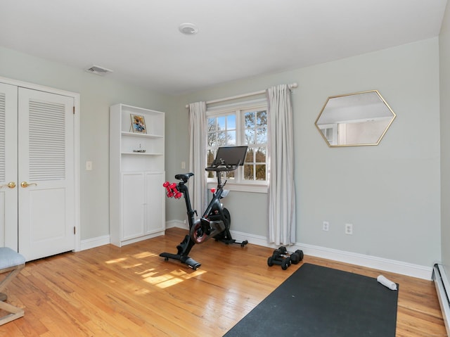 workout room with baseboards, visible vents, baseboard heating, and wood finished floors