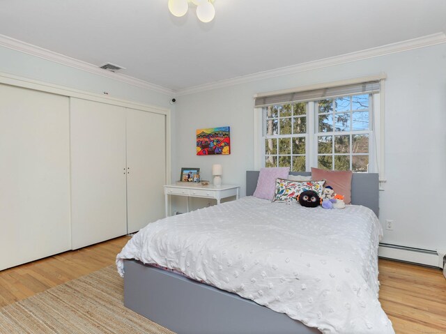 bedroom featuring visible vents, crown molding, a closet, wood finished floors, and a baseboard heating unit