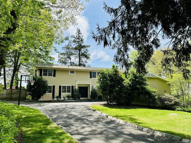 colonial home with fence, driveway, and a front lawn