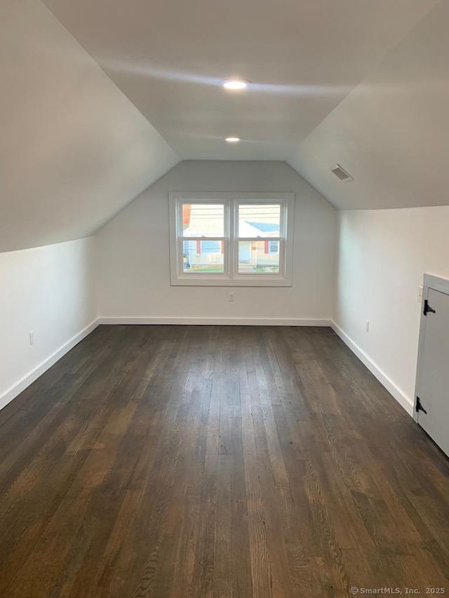 additional living space featuring baseboards, lofted ceiling, dark wood-style floors, and visible vents