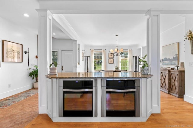 kitchen with dark stone countertops, light wood-style flooring, oven, and an inviting chandelier