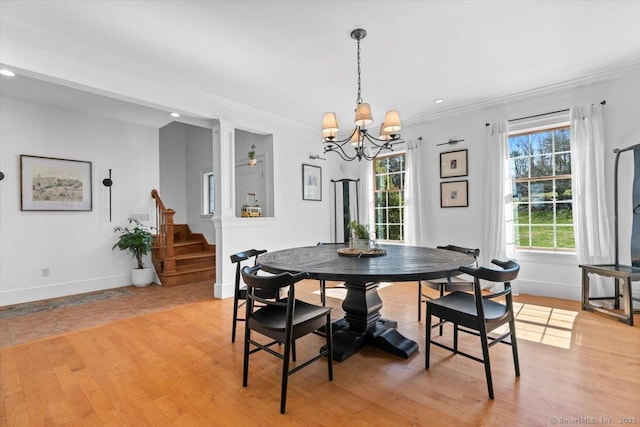 dining area with baseboards, light wood finished floors, a chandelier, and stairs
