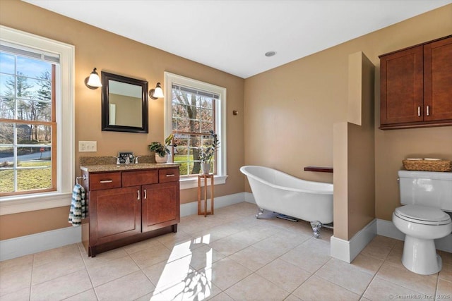 bathroom featuring toilet, a freestanding bath, baseboards, and tile patterned flooring