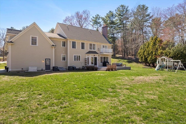 back of house featuring central AC, a yard, a playground, a balcony, and a chimney