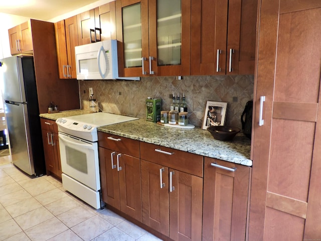 kitchen featuring tasteful backsplash, glass insert cabinets, white appliances, light stone counters, and light tile patterned floors
