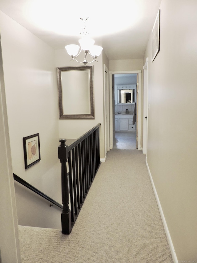 hallway featuring light carpet, an upstairs landing, baseboards, and a chandelier